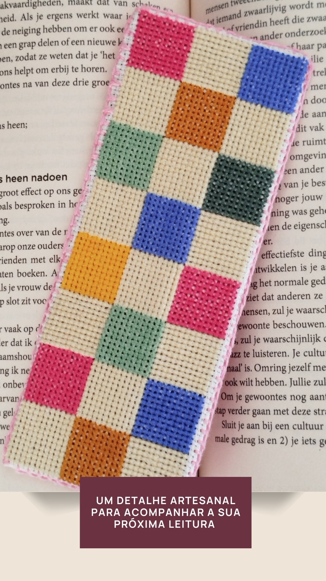 Marcador de livro bordado em ponto cruz com formas orgânicas coloridas sobre livro aberto